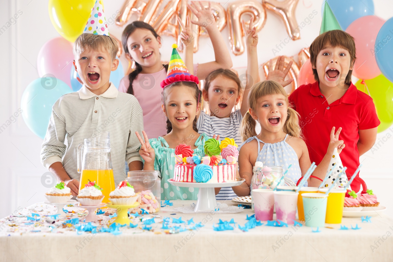 Birthday celebration. Kids at table with tasty cake and different treats in festive decorated room Photo of Birthday celebration. Kids at table with tasty cake and different treats in festive decorated room