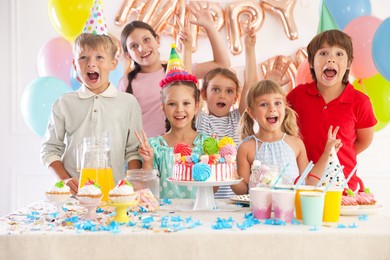 Photo of Birthday celebration. Kids at table with tasty cake and different treats in festive decorated room