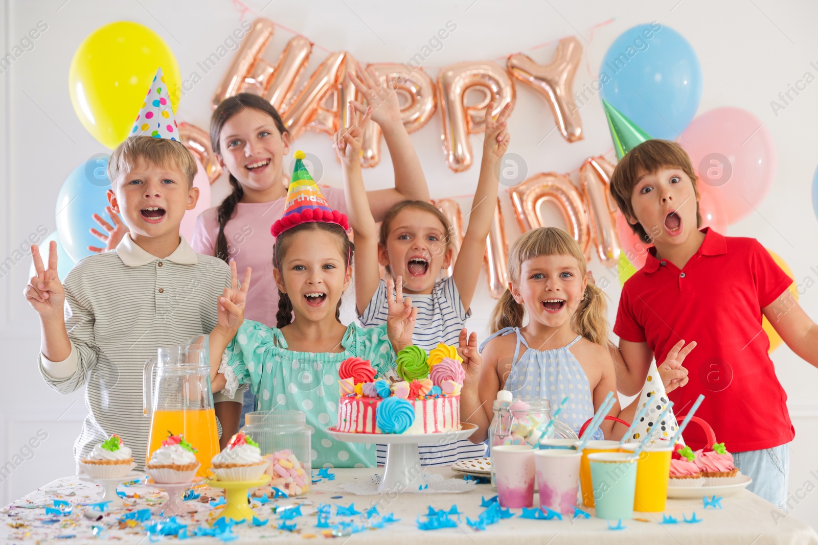 Birthday celebration. Kids at table with tasty cake and different treats in festive decorated room Photo of Birthday celebration. Kids at table with tasty cake and different treats in festive decorated room