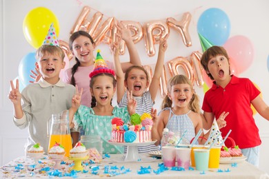 Photo of Birthday celebration. Kids at table with tasty cake and different treats in festive decorated room
