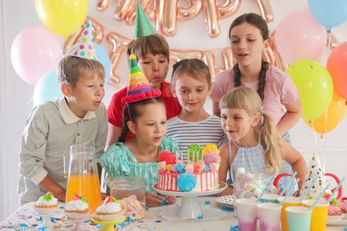 Photo of Birthday celebration. Kids at table with tasty cake and different treats in festive decorated room