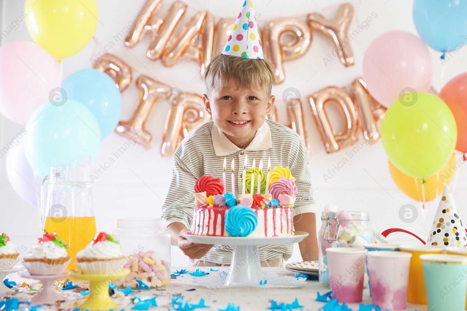 Birthday celebration. Cute little boy at table with tasty cake and different treats in festive decorated room Photo of Birthday celebration. Cute little boy at table with tasty cake and different treats in festive decorated room