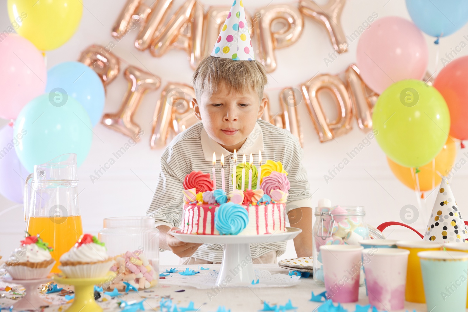 Birthday celebration. Cute little boy blowing out candles on cake at table in festive decorated room Photo of Birthday celebration. Cute little boy blowing out candles on cake at table in festive decorated room
