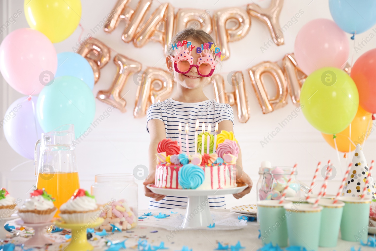 Birthday celebration. Cute little girl at table with tasty cake and different treats in festive decorated room Photo of Birthday celebration. Cute little girl at table with tasty cake and different treats in festive decorated room
