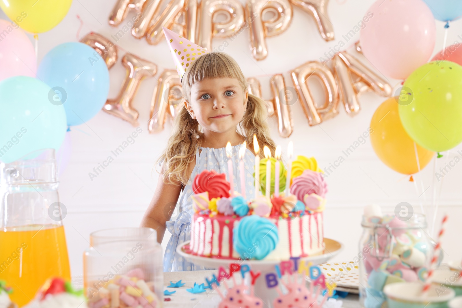 Birthday celebration. Cute little girl at table with tasty cake and different treats in festive decorated room Photo of Birthday celebration. Cute little girl at table with tasty cake and different treats in festive decorated room