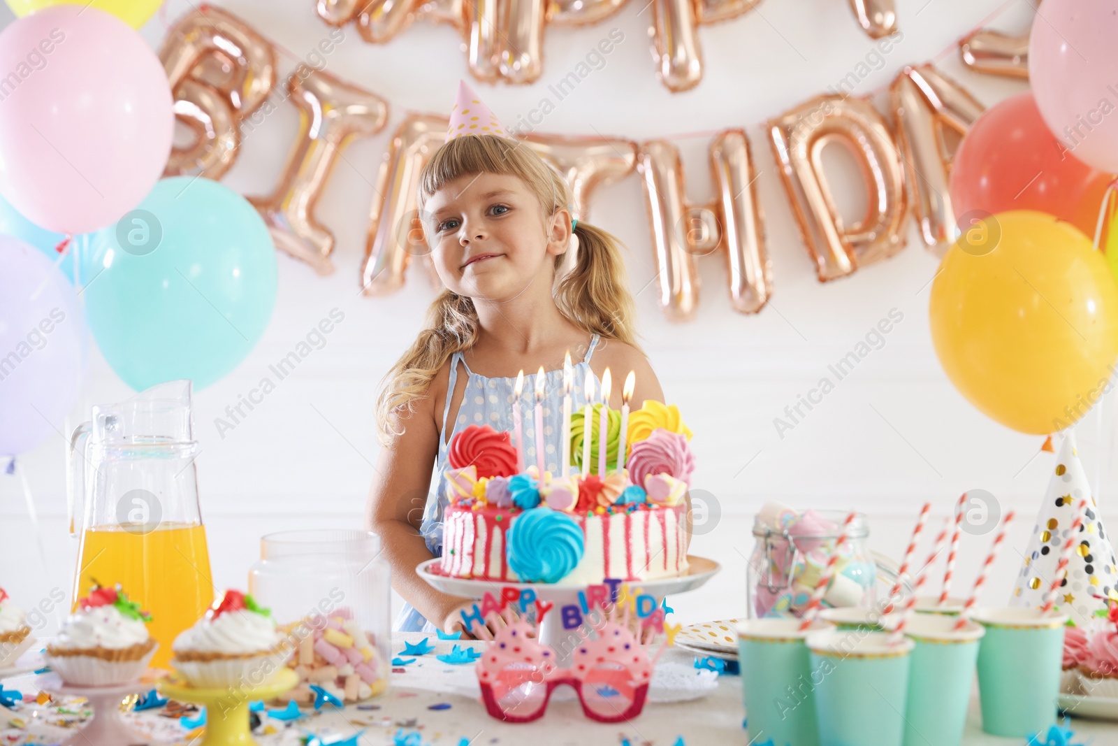 Birthday celebration. Cute little girl at table with tasty cake and different treats in festive decorated room Photo of Birthday celebration. Cute little girl at table with tasty cake and different treats in festive decorated room
