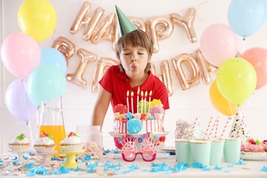 Photo of Birthday celebration. Cute little boy blowing out candles on cake at table in festive decorated room