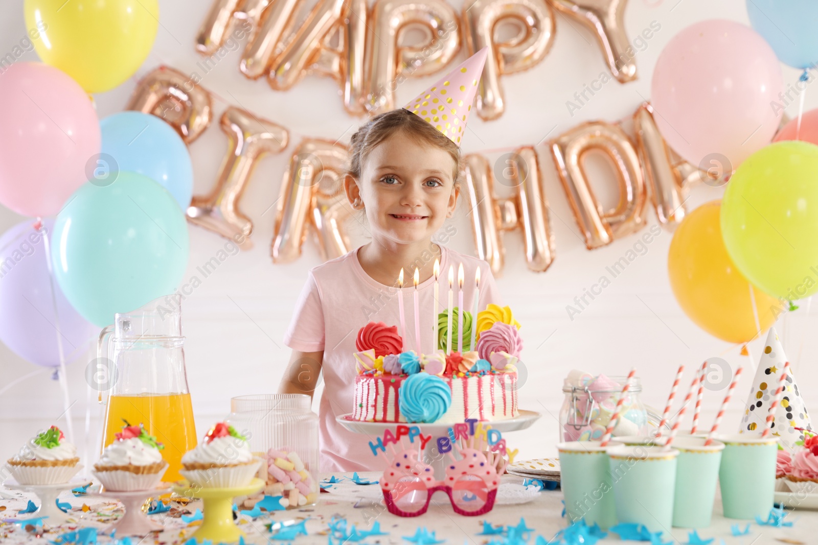 Birthday celebration. Cute little girl at table with tasty cake and different treats in festive decorated room Photo of Birthday celebration. Cute little girl at table with tasty cake and different treats in festive decorated room