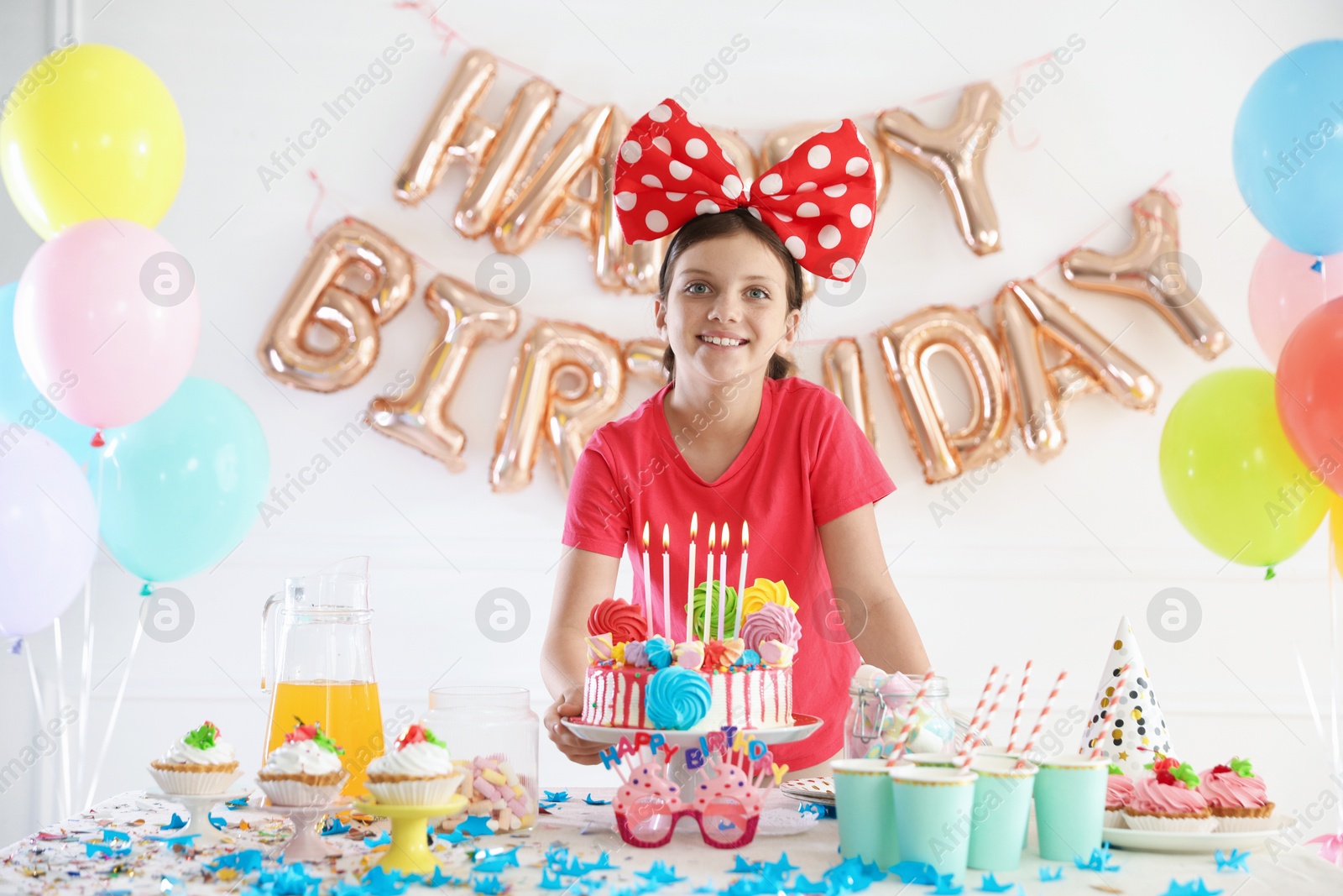 Birthday celebration. Cute girl at table with tasty cake and different treats in festive decorated room Photo of Birthday celebration. Cute girl at table with tasty cake and different treats in festive decorated room