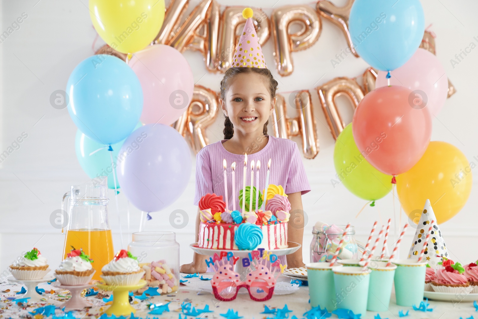 Birthday celebration. Cute little girl at table with tasty cake and different treats in festive decorated room Photo of Birthday celebration. Cute little girl at table with tasty cake and different treats in festive decorated room