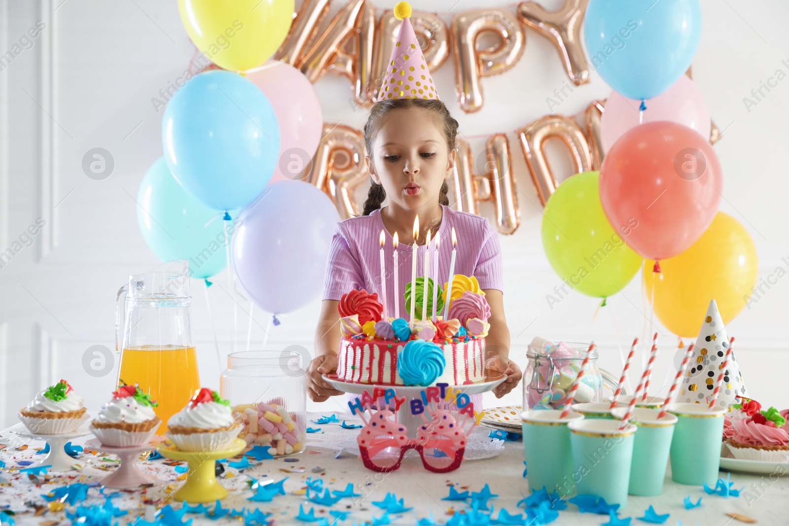 Birthday celebration. Cute little girl blowing out candles on cake and different treats in festive decorated room Photo of Birthday celebration. Cute little girl blowing out candles on cake and different treats in festive decorated room