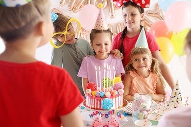 Photo of Birthday celebration. Kids at table with tasty cake and different treats in festive decorated room