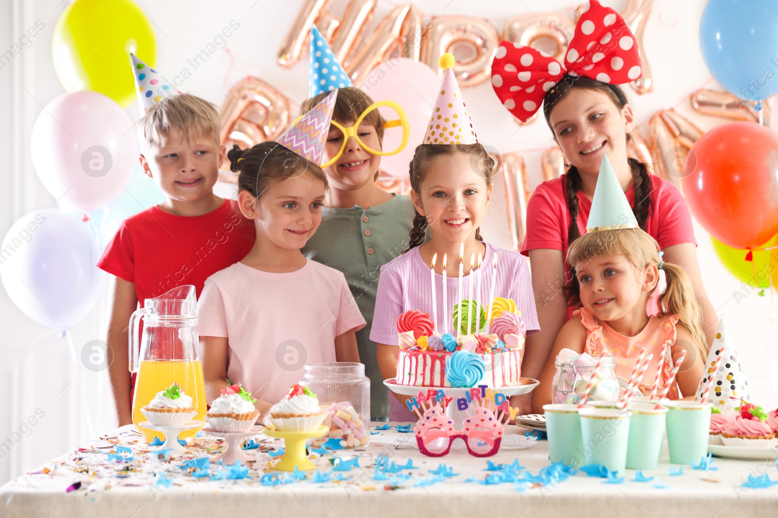 Birthday celebration. Kids at table with tasty cake and different treats in festive decorated room Photo of Birthday celebration. Kids at table with tasty cake and different treats in festive decorated room