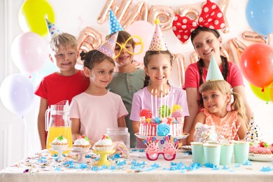 Photo of Birthday celebration. Kids at table with tasty cake and different treats in festive decorated room