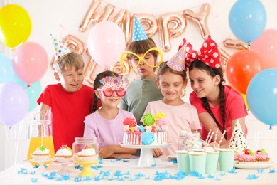 Photo of Birthday celebration. Kids at table with tasty cake and different treats in festive decorated room