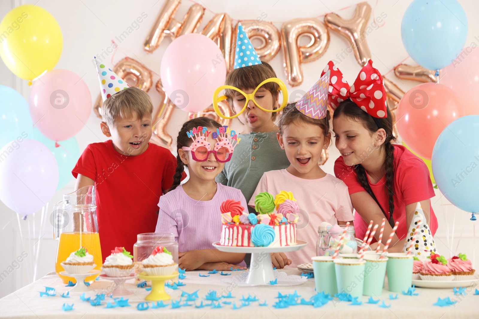 Birthday celebration. Kids at table with tasty cake and different treats in festive decorated room Photo of Birthday celebration. Kids at table with tasty cake and different treats in festive decorated room