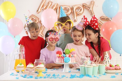 Photo of Birthday celebration. Kids at table with tasty cake and different treats in festive decorated room