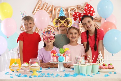 Photo of Birthday celebration. Kids at table with tasty cake and different treats in festive decorated room