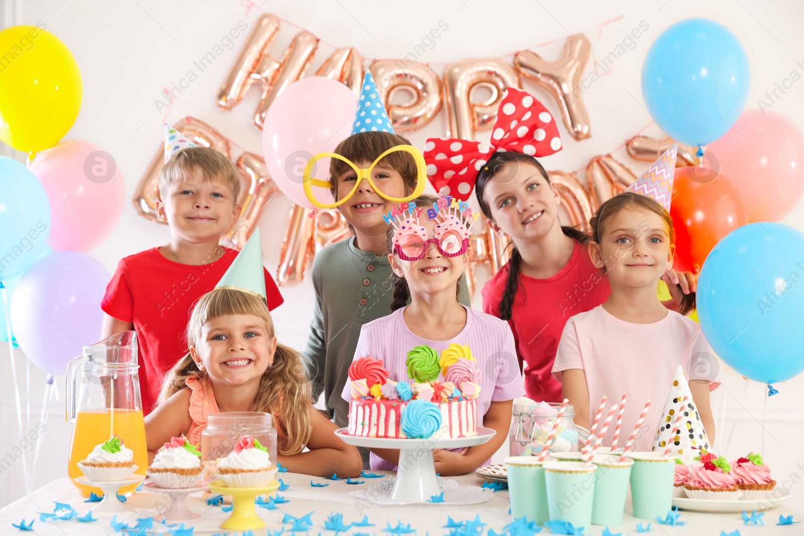 Birthday celebration. Kids at table with tasty cake and different treats in festive decorated room Photo of Birthday celebration. Kids at table with tasty cake and different treats in festive decorated room
