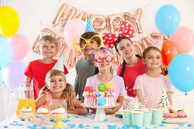 Photo of Birthday celebration. Kids at table with tasty cake and different treats in festive decorated room