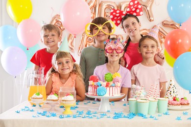 Photo of Birthday celebration. Kids at table with tasty cake and different treats in festive decorated room