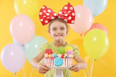 Photo of Birthday celebration. Cute little girl with tasty and balloons on orange background