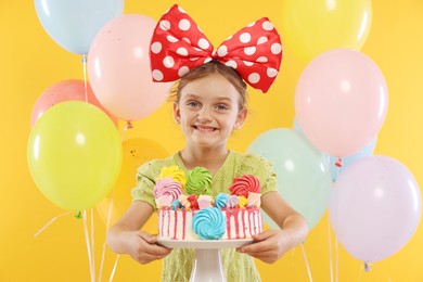 Photo of Birthday celebration. Cute little girl with tasty and balloons on orange background