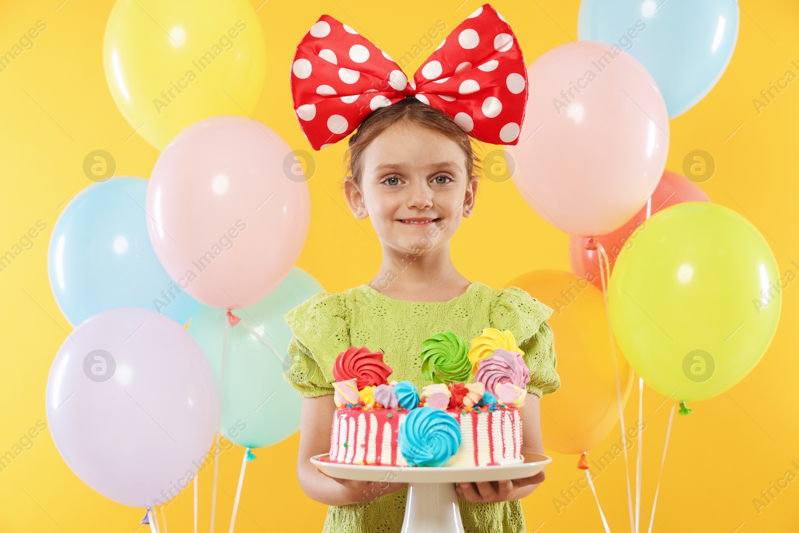 Birthday celebration. Cute little girl with tasty and balloons on orange background Photo of Birthday celebration. Cute little girl with tasty and balloons on orange background