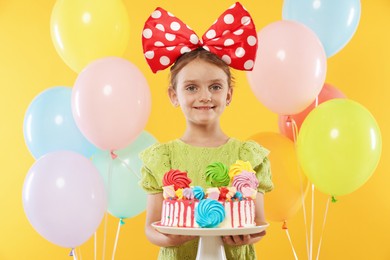 Photo of Birthday celebration. Cute little girl with tasty and balloons on orange background