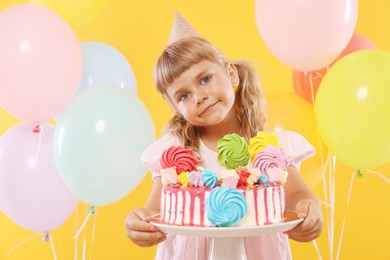 Photo of Birthday celebration. Cute little girl with tasty and balloons on orange background