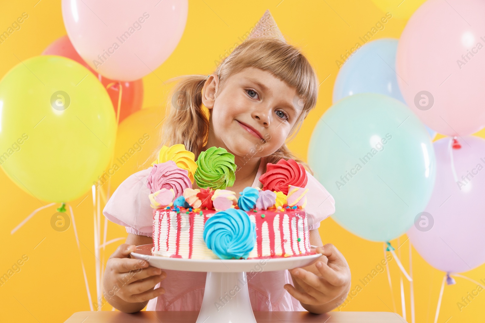 Birthday celebration. Cute little girl with tasty and balloons on orange background Photo of Birthday celebration. Cute little girl with tasty and balloons on orange background