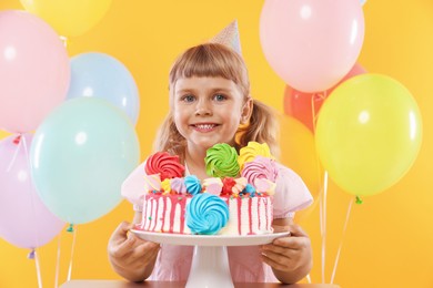 Photo of Birthday celebration. Cute little girl with tasty and balloons on orange background