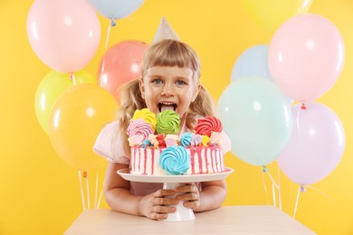 Photo of Birthday celebration. Cute little girl with tasty and balloons on orange background