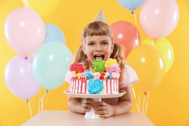 Photo of Birthday celebration. Cute little girl with tasty and balloons on orange background