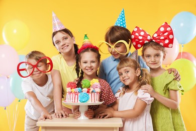 Photo of Birthday celebration. Happy kids with tasty cake and festive decor on orange background