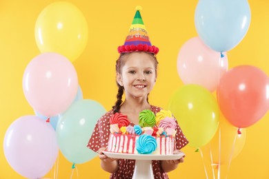 Photo of Birthday celebration. Cute little girl with tasty and balloons on orange background