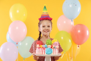 Photo of Birthday celebration. Cute little girl with tasty and balloons on orange background