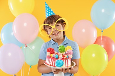 Photo of Birthday celebration. Cute little boy with tasty and balloons on orange background