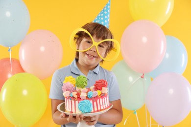 Photo of Birthday celebration. Cute little boy with tasty and balloons on orange background