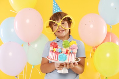 Photo of Birthday celebration. Cute little boy with tasty and balloons on orange background