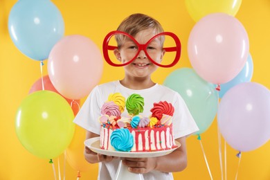Photo of Birthday celebration. Cute little boy with tasty and balloons on orange background