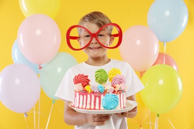 Photo of Birthday celebration. Cute little boy with tasty and balloons on orange background