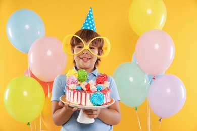 Photo of Birthday celebration. Cute little boy with tasty and balloons on orange background