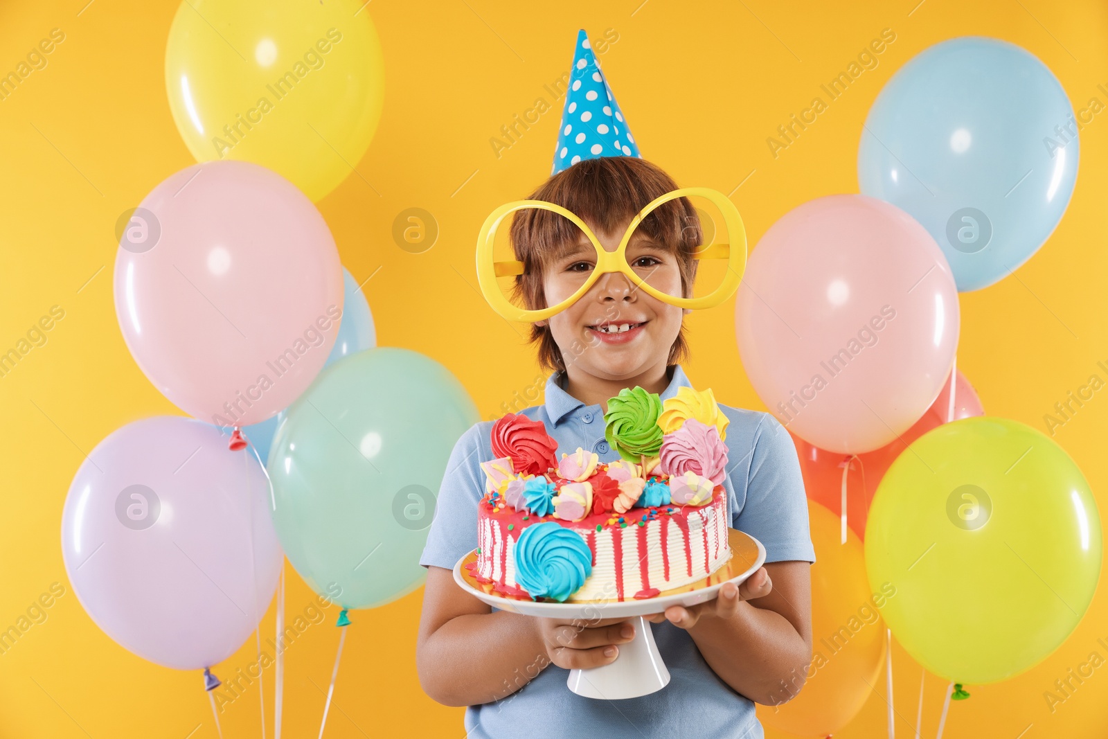 Birthday celebration. Cute little boy with tasty and balloons on orange background Photo of Birthday celebration. Cute little boy with tasty and balloons on orange background