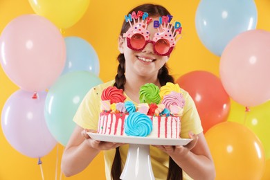Photo of Birthday celebration. Cute little girl with tasty and balloons on orange background