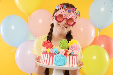 Photo of Birthday celebration. Cute little girl with tasty and balloons on orange background