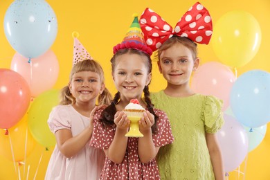 Photo of Birthday celebration. Kids with cupcake and balloons on orange background