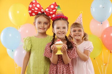 Photo of Birthday celebration. Kids with cupcake and balloons on orange background