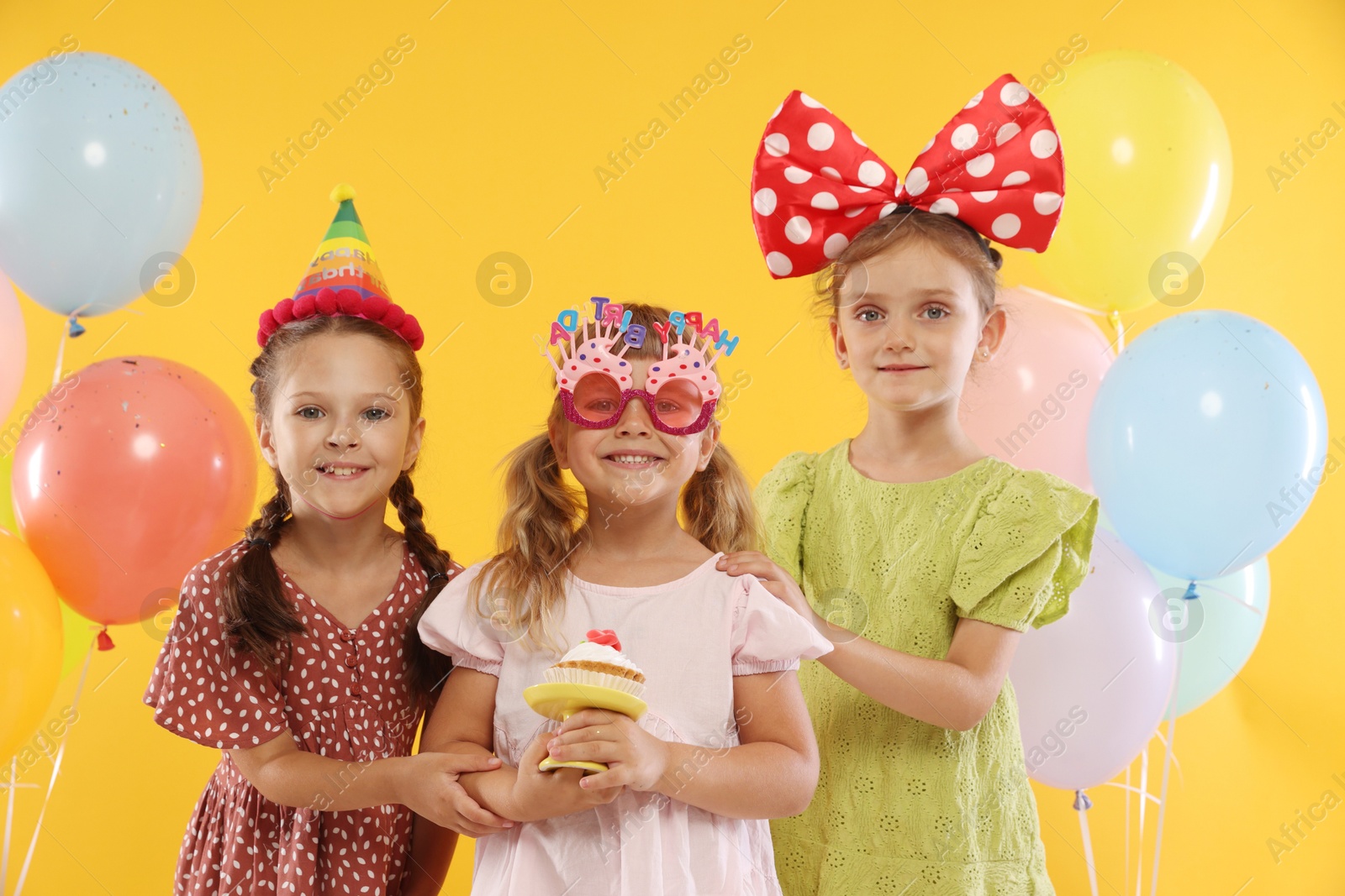 Birthday celebration. Kids with cupcake and balloons on orange background Photo of Birthday celebration. Kids with cupcake and balloons on orange background