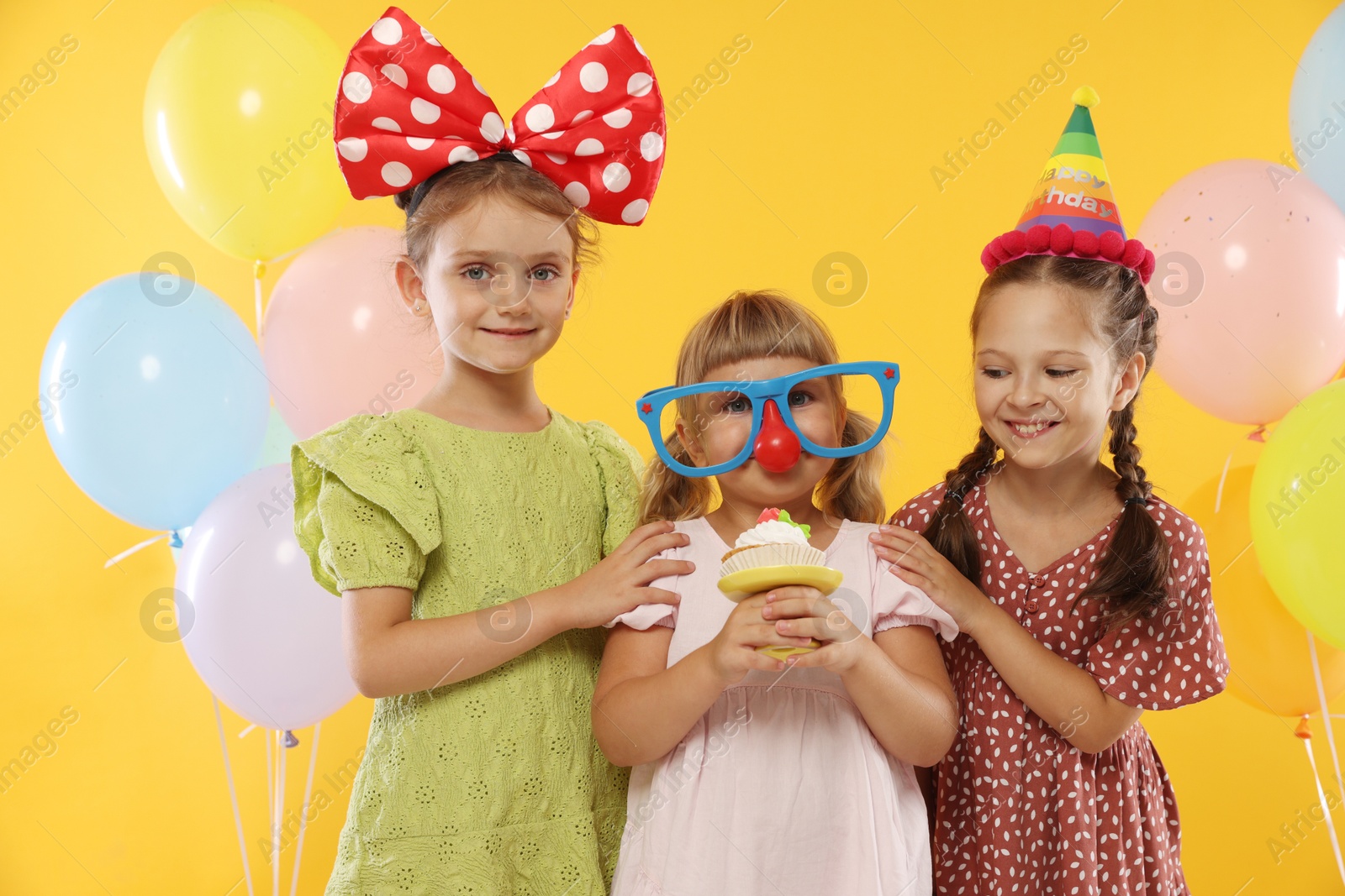 Birthday celebration. Kids with cupcake and balloons on orange background Photo of Birthday celebration. Kids with cupcake and balloons on orange background